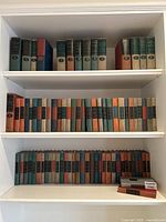 Three shelves of clothbound hardcover books displayed on a white bookshelf