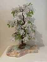 Front angle showing the bonsai tree with white quartz flowers and green stone leaves on a multicolored natural stone base.