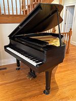 Angled view of open Yamaha baby grand piano showing legs, pedals, and lid.