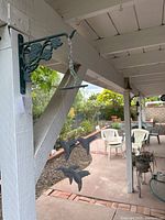 Photo of the hummingbird wind chime hanging from a floral and vine wrought iron wall bracket outside on a porch.