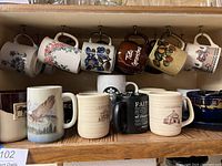 Shelf with assorted coffee cups hanging by handles and standing upright, various colors and floral/nature designs