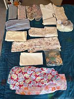 Assorted folded linens and placemats on dark quilted surface, including floral and lace pieces, some in bags