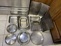 Top view of assorted baking pans placed on floor near oven showing rectangular, square, and loaf pans in stainless steel with some scuff marks.