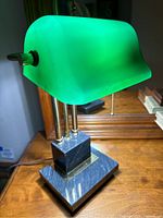 Front angled view of the bankers lamp showing green frosted glass shade, marble base, brass rods, and pull chain switch.