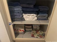 Two shelves of various colored bath towels, hand towels, dish towels, pool towels and four cloth fruit medley tapestry placemats