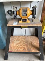 Full front view of the bench grinder mounted on the metal and wood stand, showing overall size and condition.