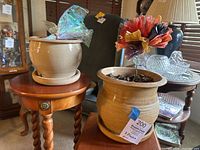 Both beige glazed ceramic planters placed on a small wooden side table, showing size and shape comparison.