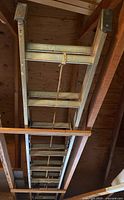Photo showing the full length of the aluminum extension ladder stored horizontally between wooden beams with attached rope pulley system.