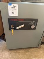 Front view of Fire Fyter fireproof safe showing combination dial, key lock with attached keys, and Fire Fyter branding.