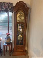 Full front view of grandfather clock showing bonnet top, dial, weights and pendulum