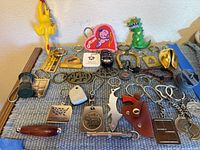 Photo showing a collection of varied keychains including the rubber chicken, Godzilla, miniature lantern, leather holster, and metal emblems.
