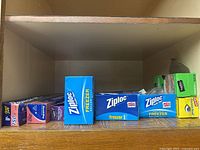 Shelf with multiple boxes of Ziploc bags including freezer and sandwich bags, and boxes of Reynolds Wrap aluminum foil and wax paper.