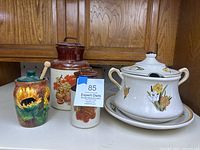 Full view of three McCoy pottery pieces: sunflower jar on left, brown and cream fruit jar center, white floral soup tureen right.