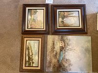 Four landscape paintings arranged on carpet: three framed including woman in wooded glen, mountain stream, rustic beach scene; one unframed rustic cottage by stream painting.