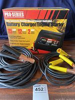 Pro-Series battery charger and engine starter with jumper cables and original box displayed in front of blue backdrop.