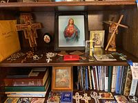 Shelf display with framed Jesus picture, wooden crosses, rosaries, medals, and religious books underneath.