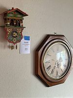 Photo showing the miniature cuckoo clock and a wooden framed wall clock side by side on a wall.