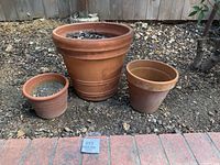 Three terracotta planters of varying sizes arranged outdoors on soil, showing size comparison and shape