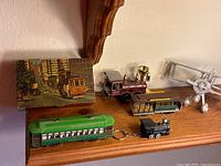 Photo showing four miniature train models and a vintage San Francisco cable car box on a wooden shelf.