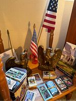 Two 1776 Eagle bronze bookends with a wooden stand holding two USA flags and multiple bundles of collector cards on a chair.