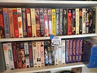 Two shelves with a wide variety of VHS tapes including movies, series and blank tapes.