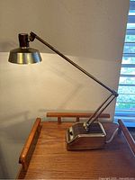 Full view of vintage brass desk lamp on wooden surface showing adjustable arm and switch base.
