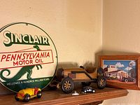 Sinclair Pennsylvania Motor Oil metal wall sign displayed behind wooden vintage-style model car and three small die-cast cars on shelf.