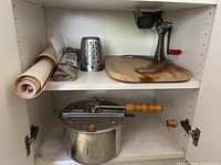 Shelf with vintage metal grinder mounted on wooden board and 3 metal cutting wheels placed on the board. Also visible are rolls of shelf paper and a kitchen towel.