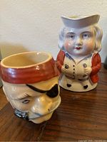 Front and side view of Toby jug ceramic mug with colonial style face and red coat, positioned behind the pirate mug