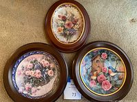 Three vintage floral-themed framed plates displayed on the floor, showing overall appearance and frame style