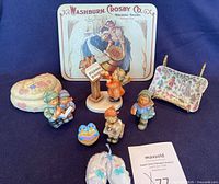 Photo of all items in the lot including Goebel Hummel figurines, trinket dish, trinket box, knitted booties, and singing bird figurine.