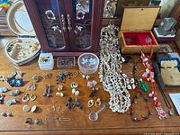 Multiple pairs of earrings, several necklaces with faux pearls and beads, and jewelry boxes on a wooden surface