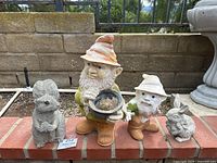 Set of four garden statues: two gnomes, squirrel, and rabbit on a brick ledge against a garden background.