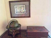 Vintage globe on wooden stand, framed map art on wall, and wooden box on table surface.