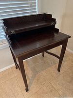 Desk shown with fold-down top open revealing storage area underneath and carved detailing around edges.