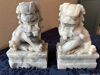 Pair of white marble Asian dragon bookends on dark cloth, showing prominent gray veining and carved details front and side views.