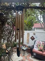 Full view of the wind chime hanging outdoors with visible brass tubes and black wooden top and wind catcher