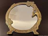 Full front view of the round bronze framed mirror with a female figure on the right side and floral accents, showing the detailed bronze work and reflective surface.