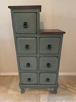 Front view of blue multi-drawer cabinet showing stepped design and nine drawers with black ring pulls.