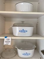 Shelf view showing three Corning Ware casseroles with lids and extra lid on left
