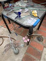 Copper dragonfly mister, stained glass butterflies, pink flower stake, and hearts on a black table.