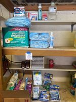 Overview of multiple shelves with packages of protective underwear, baby wipes, bandages, disinfectant, cotton balls, and boxed goods on wooden shelving.