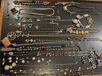 Jewelry lot laid out on flat black surface with multiple long necklaces, earrings, and pendants visible.