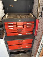 Front view of stacked red drawer cabinets with white handles, showing multiple labeled drawers and closed top section with a red knob on side