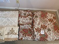 Overview of all bedding and towels included in the lot showing paisley duvet and pillows, beige fringe pillows, and decorative towels.