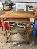 Wooden rolling butcher block cart showing the top, slatted shelf underneath, caster wheels including locking ones, and surrounding storage area.