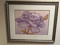 Framed floral print showing a large, detailed purple rose with accompanying rosebud and stem in soft colors, under glass and in a decorative silver frame.