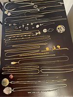 Overview of all silver and gold-tone necklaces, pendants, earrings and brooches laid out on dark surface
