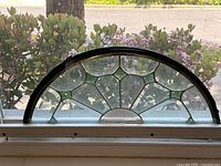 Front view of half-circle stained glass panel showing clear textured glass and black metal frame.