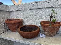 Three outdoor terracotta planters arranged on a shelf showing their shape and natural weathering.